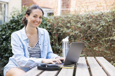 Lächelnde Unternehmerin mit Laptop im Garten - WPEF04310