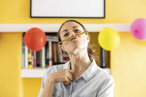 Mittlere erwachsene Frau mit Bleistift, der die Lippen zu Hause aufreißt - WPEF04329