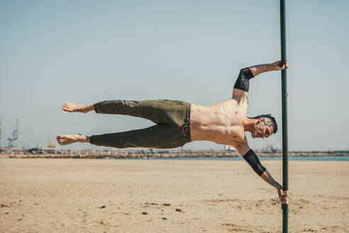 Männlicher Sportler bei einer Übung, während er am Strand auf einer Stange balanciert - ACPF01215