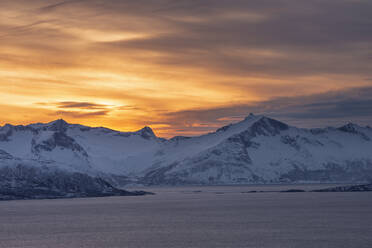 Norwegen, Tromso, Kvaloya, Dramatischer Himmel über dem schneebedeckten Berg Senja Island von der Insel Kvaloya aus gesehen bei Sonnenuntergang - RUEF03268