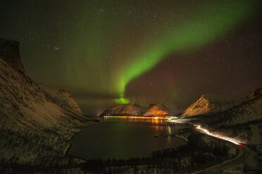 Norwegen, Tromso, Bergsbotn, Blick auf die Aurora Borealis über dem beleuchteten Fjorddorf auf der Insel Senja - RUEF03279