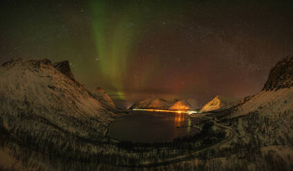 Norwegen, Tromso, Bergsbotn, Blick auf die Aurora Borealis über dem beleuchteten Fjorddorf auf der Insel Senja - RUEF03280