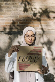 Schöne Frau hält Plakat mit Gleichstellung Text vor der Wand - XLGF01574