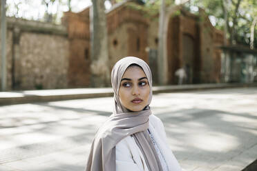 Junge Frau mit Hidschab, die auf dem Gehweg sitzt und wegschaut - XLGF01581