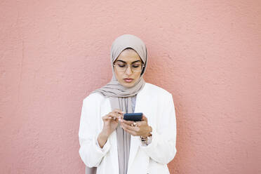 Junge Frau, die ein Smartphone benutzt, während sie vor einer rosa Wand steht - XLGF01589