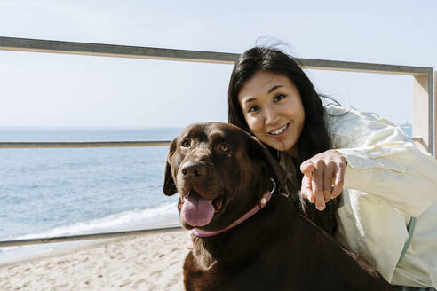 Schöne Frau mit Labrador-Hund, der auf einen sonnigen Tag am Strand zeigt - AFVF08653