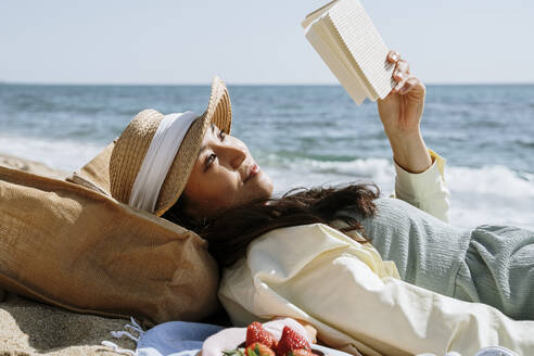 Frau liest ein Buch, während sie am Wochenende am Strand liegt - AFVF08665