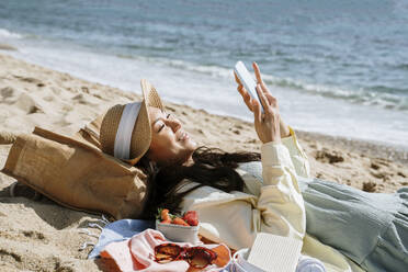 Frau benutzt Smartphone, während sie am Strand im Sand liegt - AFVF08668