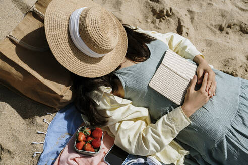 Frau bedeckt ihr Gesicht mit einem Hut, während sie am Strand liegt - AFVF08669