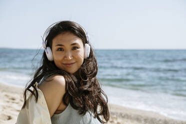 Beautiful woman wearing headphones smiling at beach on sunny day - AFVF08672