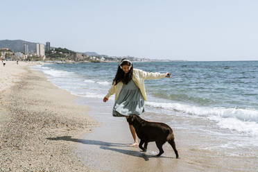 Woman playing with Labrador dog at beach during weekend - AFVF08674