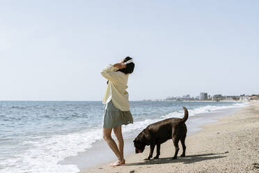 Frau hört Musik über Kopfhörer bei einem Hund am Strand - AFVF08675