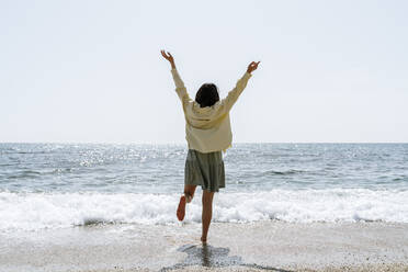 Frau mit erhobenen Armen am Strand stehend an einem sonnigen Tag - AFVF08678