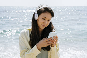 Frau mit Kopfhörern und Smartphone am Strand - AFVF08682