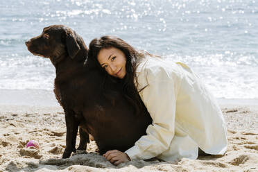 Beautiful woman embracing dog on sand during sunny day - AFVF08686