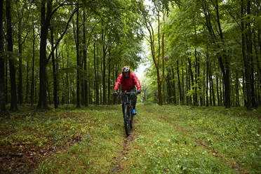 Männlicher Sportler in Sportkleidung beim Fahrradfahren auf einem Waldweg - PMF01784