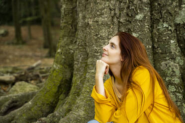 Junge Frau träumt bei einem großen Baumstamm im Wald - AFVF08690
