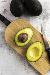Studio shot of kitchen knife and halved avocado lying on cutting board - GIOF12516