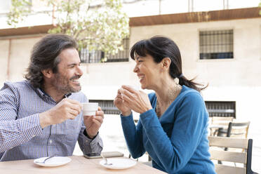 Happy mature couple smiling while having coffee at terrace - JCCMF02004