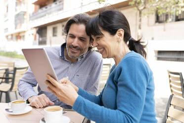 Ehepaar, das auf der Terrasse sitzend ein digitales Tablet benutzt - JCCMF02005