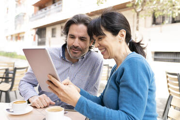 Mann und Frau benutzen ein digitales Tablet auf einer Terrasse - JCCMF02006