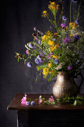 Bunte blühende Blumen auf dünnen Stielen auf Vase auf Holztisch in Haus auf grauem Hintergrund - ADSF23195