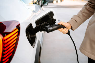 Crop of stylish male entrepreneur browsing smartphone while standing at petrol station and refueling automobile - ADSF23198