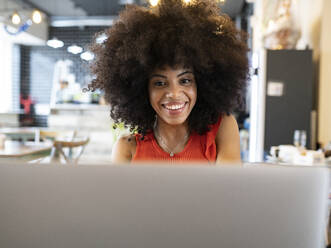 Zufriedene schwarze Freiberuflerin, die in einem Café sitzt und auf ihrem Netbook surft, während sie aus der Ferne an einem Online-Projekt arbeitet - ADSF23273