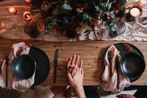 Oben Ansicht der Ernte anonymen Bräutigam und Braut hält die Hände auf serviert Tisch mit Blumendekor und brennenden Kerzen im Restaurant - ADSF23281