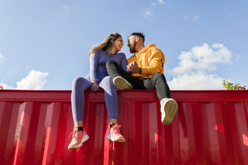 Junges Paar hält sich an den Händen und sitzt auf einem roten Container - JRVF00470