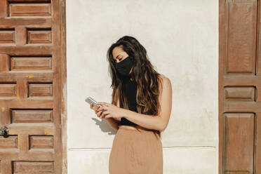 Female tourist wearing protective face mask while using mobile phone during sunny day - MRRF01041