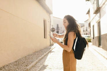 Young tourist with backpack using mobile phone while standing on road - MRRF01047