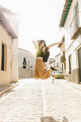 Young carefree woman with arms outstretched jumping on footpath - MRRF01049