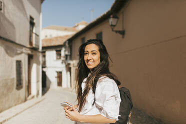 Weibliche Touristin mit Rucksack und Mobiltelefon an einem sonnigen Tag - MRRF01052