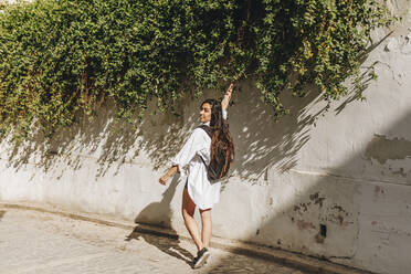 Tourist with backpack touching plant on surrounding wall - MRRF01068