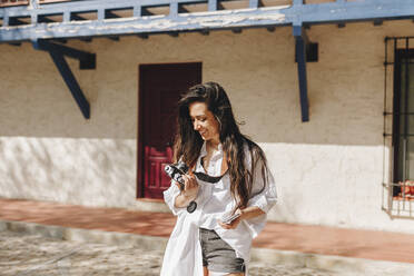 Frau lächelt, während sie die Kamera in einem Dorf an einem sonnigen Tag hält - MRRF01083