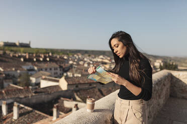 Weibliche Touristin prüft eine Landkarte, während sie an einer Stützmauer steht - MRRF01090