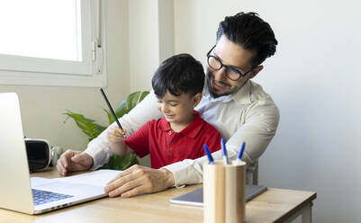 Geschäftsmann schaut auf einen Laptop, während er mit seinem Sohn zu Hause sitzt - JCCMF02008