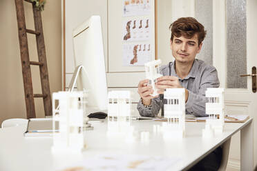 Männlicher Architekt, der an einem Tisch sitzend ein Architekturmodell untersucht - UKOF00144