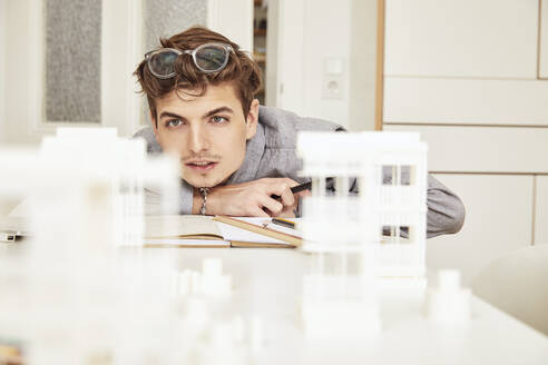 Männlicher Architekt, der sich auf ein architektonisches Modell konzentriert, während er an einem Tisch arbeitet - UKOF00149