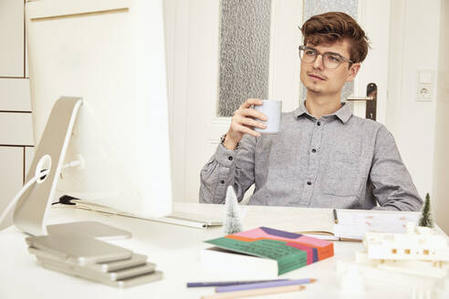 Männlicher Architekt schaut auf den Computer, während er am Tisch Kaffee trinkt - UKOF00151