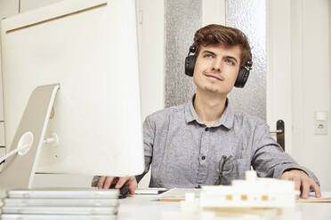 Männlicher Architekt schaut weg, während er im Büro über Kopfhörer Musik hört - UKOF00154