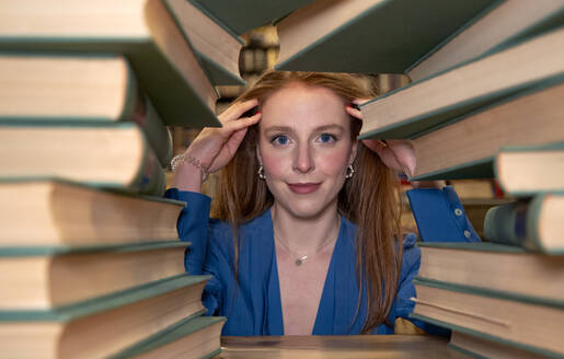 Attractive young woman seen through stack of books in library - VEGF04338