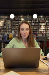 Beautiful woman using laptop in library - VEGF04362