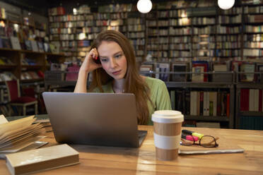 Junge Frau studiert in einer Bibliothek mit Laptop - VEGF04364