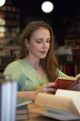 Junge Frau konzentriert sich beim Lesen eines Buches in einer Bibliothek - VEGF04372