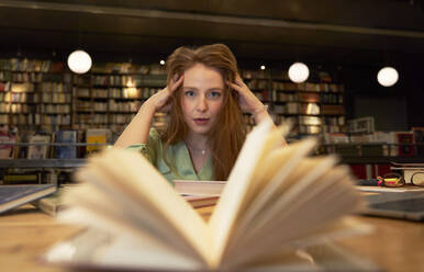 Erschöpfte Frau mit Hand im Haar in der Bibliothek - VEGF04378