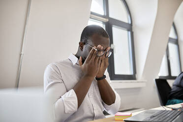 Müder männlicher Unternehmer, der sich die Augen reibt, während er im Büro sitzt - ZEDF04148