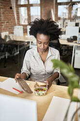 Afro businesswoman opening container during lunch break at office - ZEDF04168