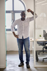 Smiling businessman leaning at doorway in office - ZEDF04186